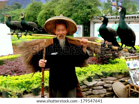 Yangshou, China - April 29, 2006:  Bearded Chinese man wearing straw hat holding bamboo pole with four cormorant birds