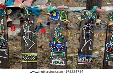 Lijiang, China - April 21, 2006:  Hand-painted figures of mythical animals & stick people decorate a fence hung with miniature straw hats and bells at Dongba Wan Shen (God\'s Garden) historic site