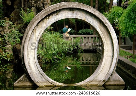 Chengdu, China - May 8, 2008: Man reading a book viewed through a traditional Chinese moon gate in the gardens of the Manjursi Monastery at the Wenshu Buddhist Temple