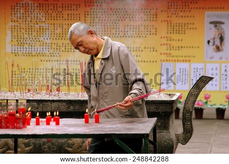 Chengdu, China - September 20, 2006:  An elderly Chinese man lighting incense sticks from burning red candles at the Da Ci Buddhist Temple