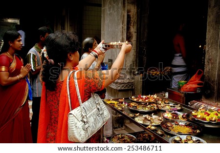 Singapore - December 16, 2007:  Woman makes an offering with a silver bowl containing food and lighted candles at the Sri Veeramakaliamman Hindu Temple in Little India