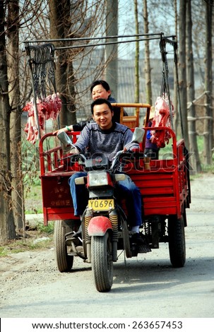 Wan Jia, China - February 12, 2009:  Mother and son driving their motorcycle portable butcher shop truck along a country road selling fresh cuts of pork