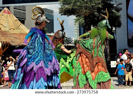 Bangkok, Thailand - January 11, 2013:  A trio of stilt-walking performers manipulate their giant antelope puppets entertaining crowds in the Siam Paragon & Siam Center outdoor plaza on Children\'s Day