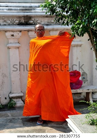 Bangkok, Thailand - December 17, 2012:  Buddhist monk wrapping an orange robe around his body in a courtyard at Wat Ratchanadda