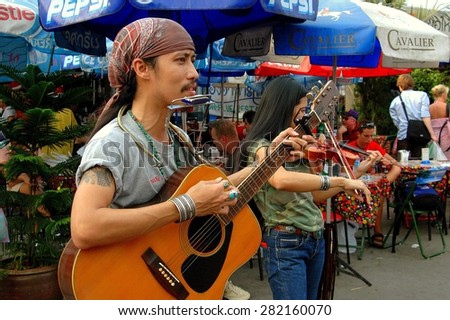 Bangkok, Thailand - December 26, 2005:  Two musicians playing a guitar and violin entertain visitors at the renowned Chatuchak weekend outdoor market