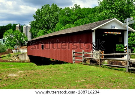 Quarryville, Pennsylvania - June 6, 2015: 19th century Mount Pleasant Road Covered Bridge with an Amish farm\'s silos in the background