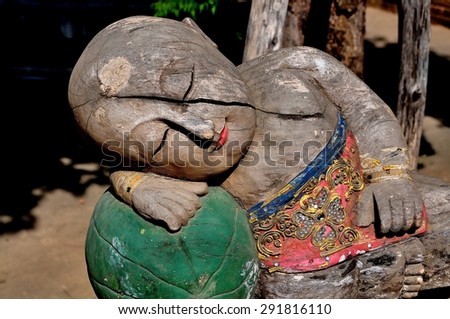 Chiang Mai, Thailand - December 21, 2012:  Carved wooden male sculpture with a crack splitting its face and chest rests on a carved green fruit at Wat Chai Mongkhol