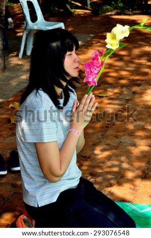 Chiang Mai, Thailand - January 3, 2013:  Thai woman kneeling in prayer holds two stems of Gladiolas in her hands at a Wat Phra Singh outdoor shrine