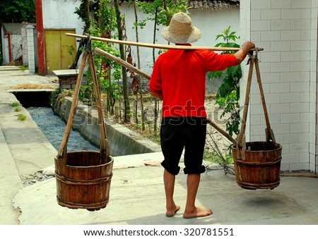 Pengzhou, China - May 7, 2007:  Farmer carrying two wooden water buckets suspended from a shoulder yoke in front of his farmhouse