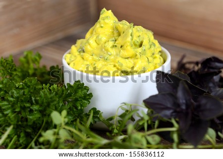 Fresh and delicious herb butter in a small bowl decorated with different kind of herbs around like red basil, parsley and rosemary. Image taken on wooden background.