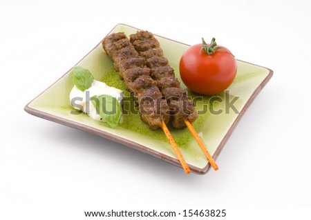 Tasteful grilled meat sticks served with tomato and garlic dip on a green plate