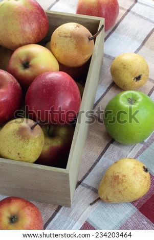 Loose apples and pears next to a box full of fruit.