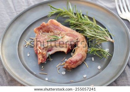 Shallow fried lamb cutlet with rosemary and sea salt on a grey tin plate.