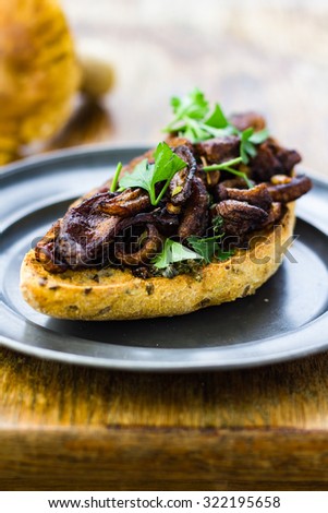 Fried wild mushrooms on toasted bread, served on a tin plate.