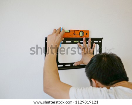 Asian technician hands holding a TV wall mount against the wall while looking for the right angle to make a mark for a drilling Сток-фото © 