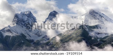Three Sisters - part of Canadian Rocky Mountains, partially covered with clouds on a chilly morning. Canmore, Alberta