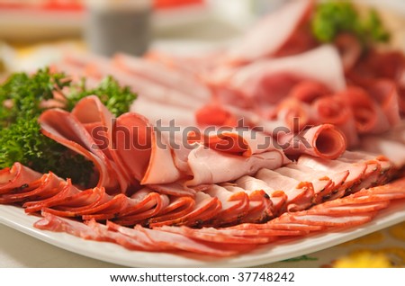 Assorted cold cuts (ham, turkey, sausage) arranged on a plate and garnished with fresh parsley leaves.