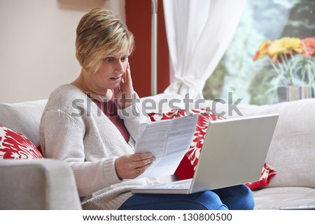 Worried woman looking at bill while on computer at home