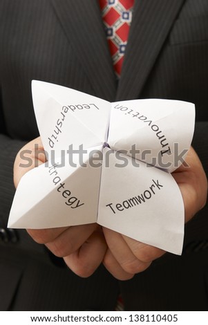 business man holding origami fortune teller with teamwork,leadership,innovation and strategy written on it