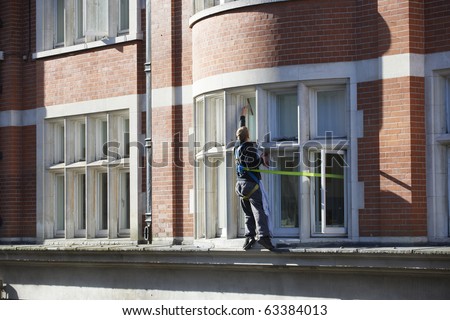 window cleaner standing on ledge with a safety harness