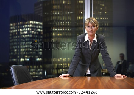 Senior Business woman leaning on table in boardroom looking at camera