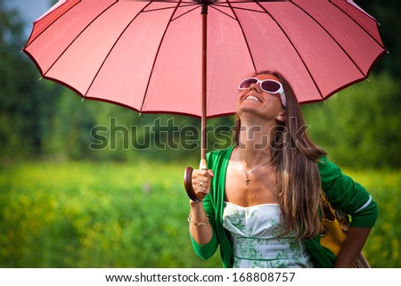 Happy young woman with umbrella under the summer rain. Beautiful girl enjoying rainy summer day looking up at sky smiling cheerful.