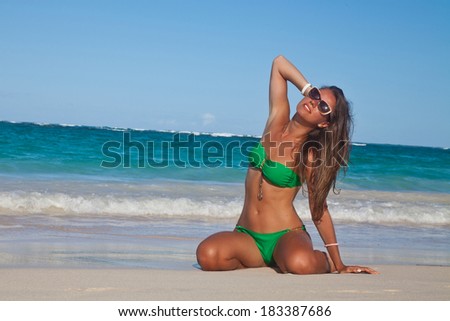 Hot sexy woman in green bikini in meditation enjoying summer sun and tanning during holidays on Hawaii. Smiling beautiful woman sunbathing on the Hawaiian beach. Travel concept.