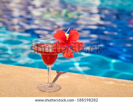 Strawberry margarita cocktail drink with hibiscus flower at the edge of the swimming pool.