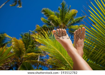 Vacation Concept. Tanning on the exotic Beach. Woman\'s Bare Feet with fashion pedicure over palms background