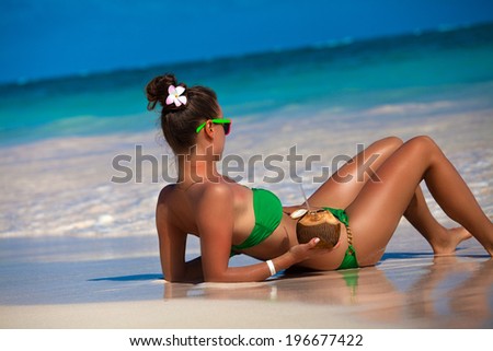 Young woman in green sexy bikini with coconut cocktail on the beach, caribbean paradise resort