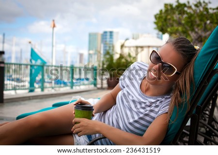 Young woman drinking coffee in a trendy resort, sitting outdoor enjoying her morning coffee. Summer luxury vacation.
