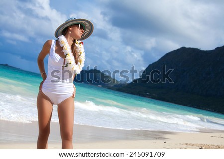 Waimanalo Beach Tourist in one of the best place in Honolulu on Oahu, Hawaii, USA. Gorgeous young woman in white bikini standing on the beach in the sunshine with welcoming Lei. Tourism Concept.