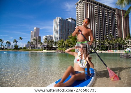 Honeymoon couple swimming in surfboard, tropical summer holiday vacation. Romantic couple joyful and full of happiness on travel vacation on Waikiki beach, Oahu, Hawaii, USA
