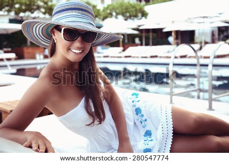 Portrait of beautiful tanned woman, relaxing beside a luxury swimming pool. Girl at travel spa resort pool. Summer luxury vacation. (focus on woman face)