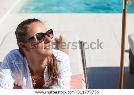 Pretty young woman with sun glasses relaxing at the luxury poolside. Girl at travel spa resort pool. Summer luxury vacation.