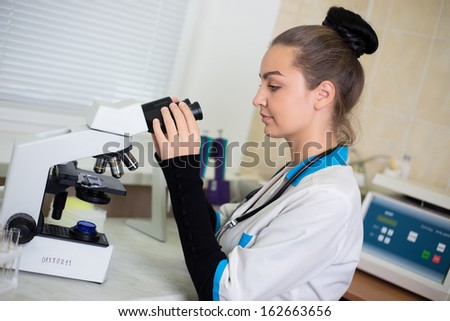 A portrait of a young beautiful woman doctor in a clinic medical laboratory with a microscope sitting