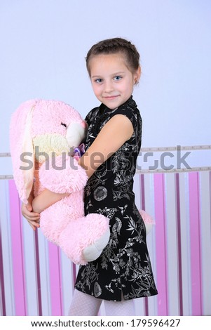 A portrait of a child girl posing in studio wearing a black dress close-up look holding a big pink bunny toy