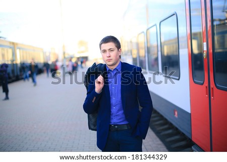 A businessman standing in front of a train holding a jacket
