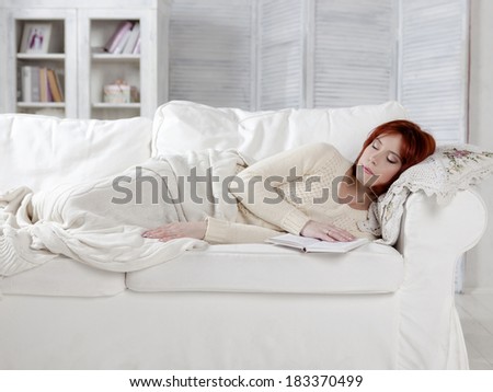 Young woman taking a nap lying on a sofa with a book