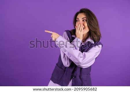 Young woman in a shirt and a vest on a purple background laughs loudly, covering her mouth with her hand, pointing her finger to the left Stock foto © 