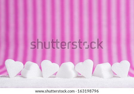 Lower thirds row of white sugar hearts on pink striped background.