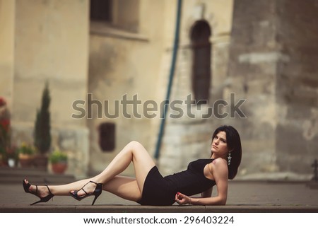 beautiful girl in a black dress stands near architectural structures, posing