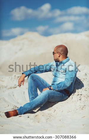 young man in glasses lies in jeans clothes on the sand in Dubai