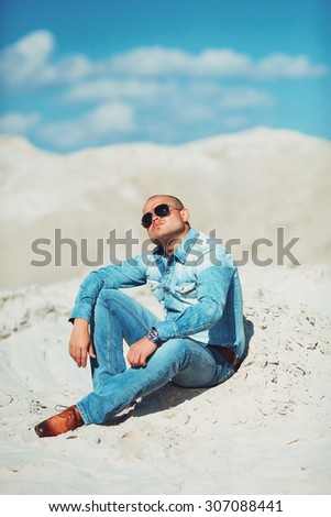 young man in glasses lies in jeans clothes on the sand in Dubai