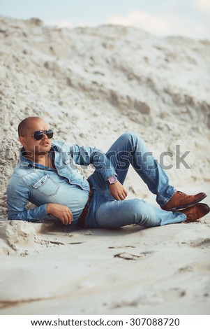 young guy in spectacles lying in jeans clothes in the sand in Egypt