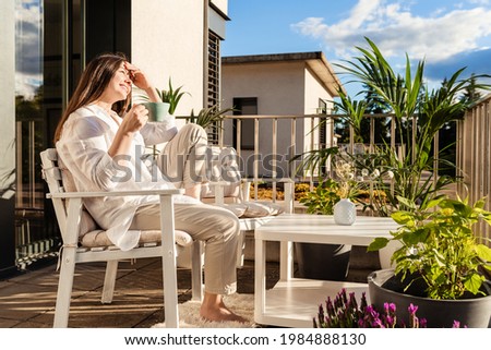 Beautiful young girl with long hair relaxing, drinking tea and enjoying sun sitting at balcony at sunlight at summer. Backyard terrace vacation. Imagine de stoc © 