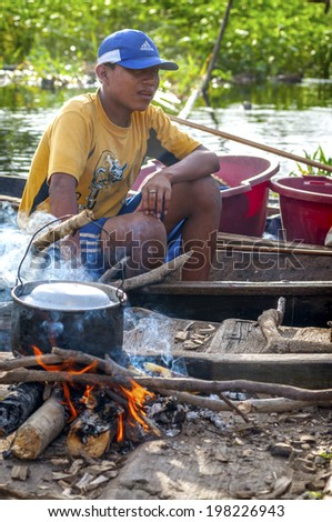 AMAZONIA, PERU - DEC 28: Unidentified Amazonian indigenous man cooking fish over a wooden raft, on December 28, 2009, in Peruvian Amazonia, Loreto, Peru, South America