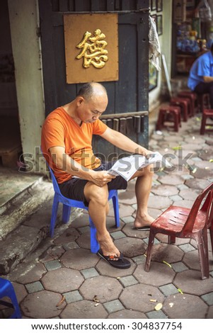 HANOI, VIETNAM - APRIL 8, 2015: Unidentified vietnamese man reading newspaper in the street, on April 8, 2015, in Hanoi, Vietnam