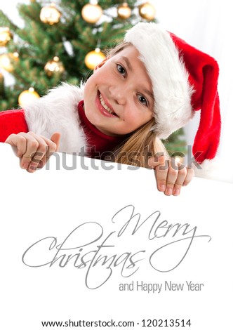 Pretty blond hair girl with santa hat and red comforter holding white board with space for text isolated on white. Christmas tree in background