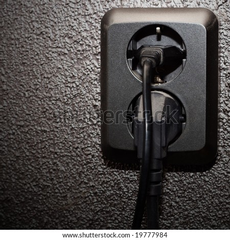 Black socket with two black plugs in dark wall